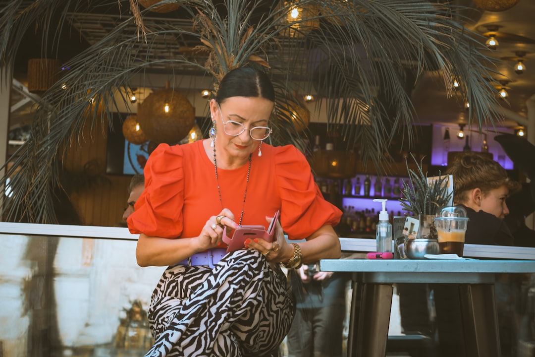 Woman in orange top uses phone at outdoor cafe