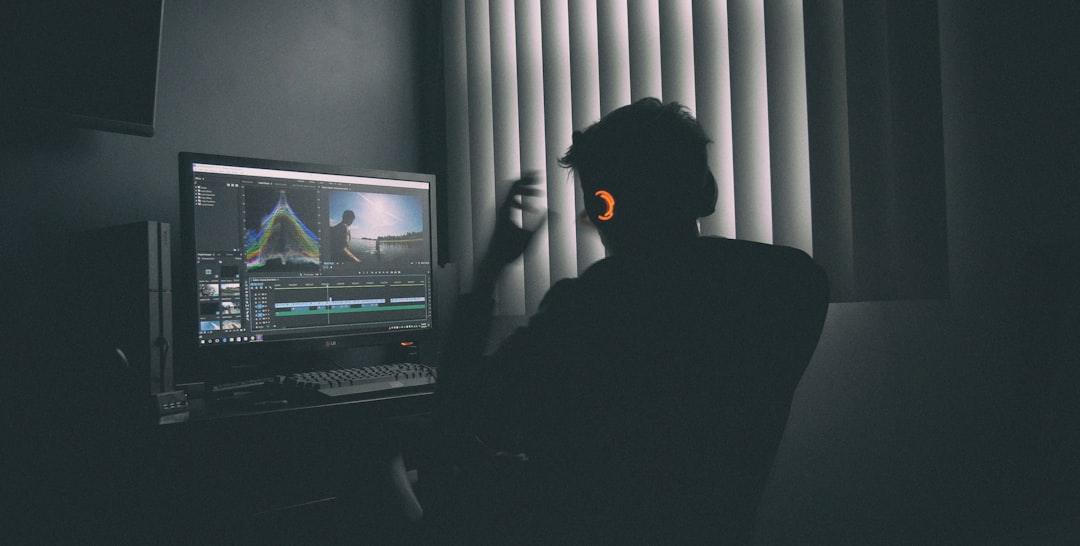 A person in silhouette wearing headphones editing video on a computer in a dark room